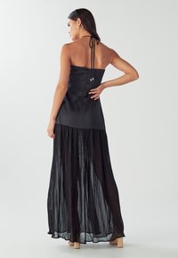 Schwarzes Maxikleid mit einem satinierten, taillierten Oberteil und einem plissierten Unterrock. Es hat eine Halter-Nackenbindung und Holzblockabsätze.