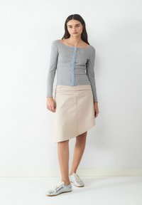 Gray long-sleeve top with button details, paired with a beige asymmetrical skirt. Model wears silver sneakers, standing against a white background.