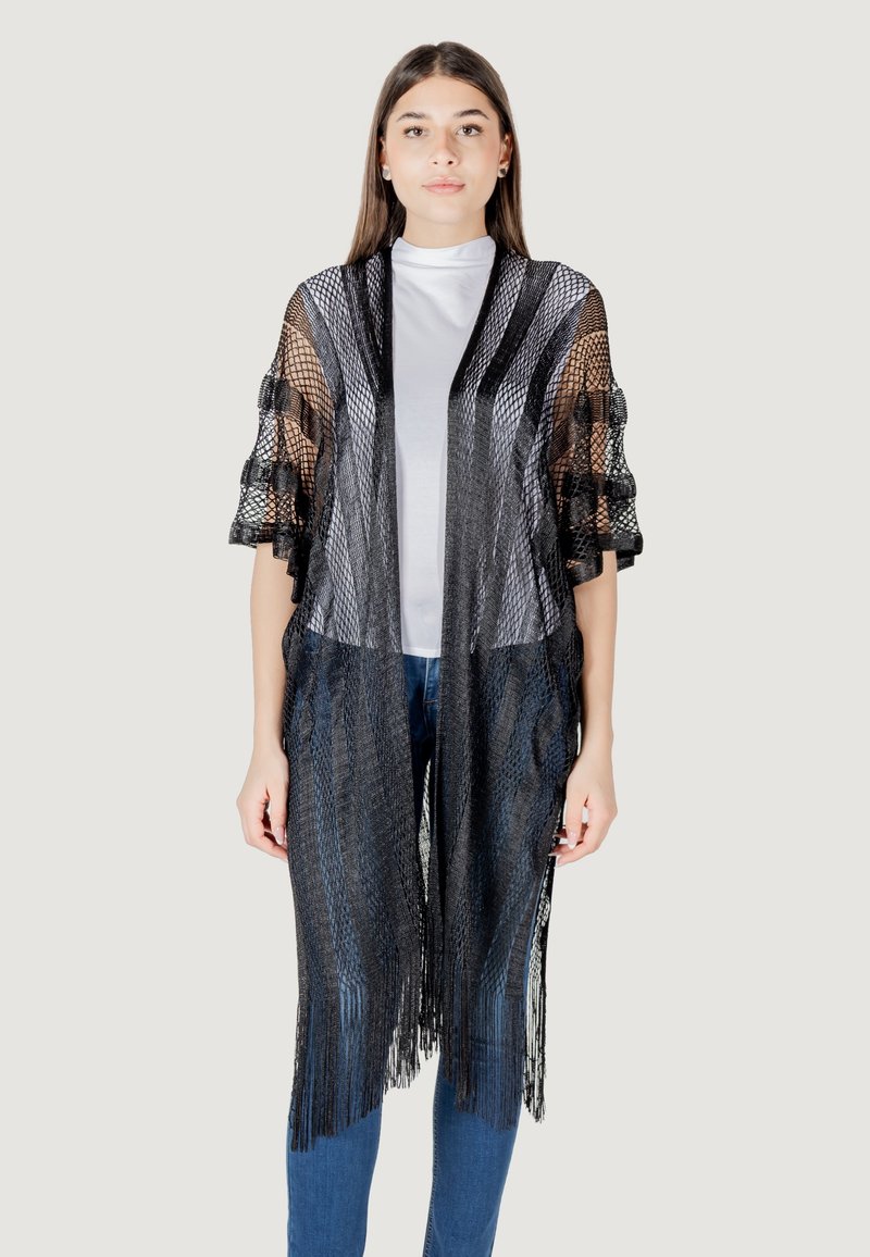 Kimono nero a maglia con maniche ampie, caratterizzato da un orlo a frange e design aperto sul davanti. Indossato sopra una maglietta bianca e jeans blu.