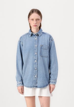 Camicia in denim azzurro chiaro, con bottoni frontali, maniche lunghe, una tasca sul petto, cuciture a contrasto, vestibilità rilassata e orlo curvo.