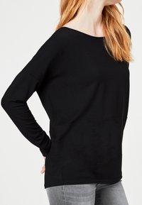 Svart långärmad skjorta med vid halsringning, lös passform och mjuk textur; har sänkta axlar och rak fåll.