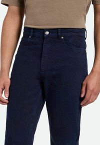 Jeans de mezclilla azul oscuro con corte recto, que cuentan con bolsillos delanteros, un cierre de botón plateado y un sutil detalle texturizado.
