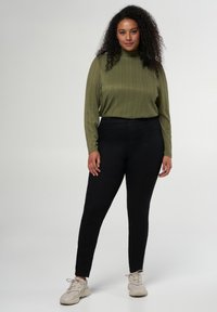 Haut à manches longues côtelé olive avec un col montant associé à un pantalon skinny noir et des baskets gris clair. Design simple et ajusté.