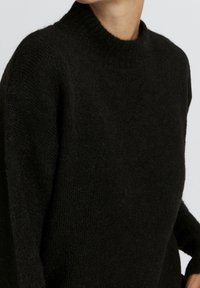 Pull en maille noir avec un col montant côtelé. Fabriqué dans un tissu doux et texturé, il présente des manches volumineuses et une coupe décontractée.