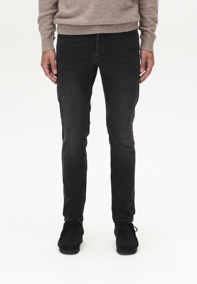 Slim-fit černé džíny s jemným vyblednutím, designem s pěti kapsami a prošitými detaily, spárované s černými botami a béžovým svetrem.