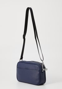 Borsa a tracolla blu navy con materiale sintetico testurizzato, forma rettangolare, accessori in argento e chiusura con zip. Cintura nera regolabile.