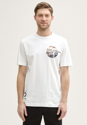 Tricou din bumbac alb cu mâneci scurte, prezentând o imprimare grafică circulară cu text negru și bej. Accente negre pe tiv.