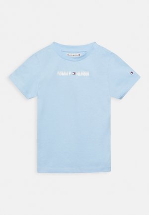 T-shirt pour tout-petit à manches courtes bleu clair avec le logo "Tommy Hilfiger" et le drapeau sur la poitrine, ainsi qu'un petit drapeau sur la manche gauche.