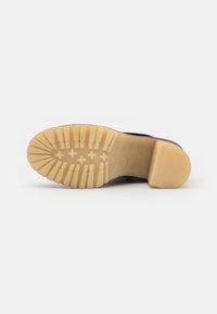 Suela de zapato de cuero marrón con una suela exterior de goma texturizada color crema que presenta estrías y surcos para mayor tracción. Tacón acampanado para estabilidad.