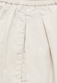 Pantalones de cintura elástica beige con pliegues frontales, que presentan una textura suave y lisa y un sutil detalle de costura en la tela.