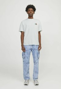 Camiseta de manga corta gris claro con un pequeño gráfico de color, combinada con jeans de carga azul claro que tienen bolsillos laterales y un corte relajado.