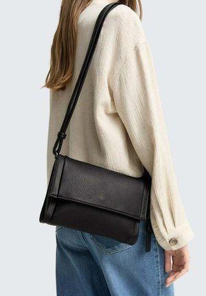 Borsa a tracolla in pelle nera con finitura testurizzata, forma rettangolare e tracolla regolabile, indossata sopra una camicia di colore chiaro.