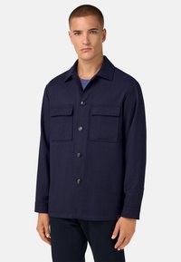 Námořnická modrá bunda s knoflíkovou přední částí, dvěma náprsními kapsami a klasickým límcem. Vyrobena z texturované tkaniny s uvolněným střihem.