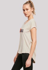 Beige t-shirt with a relaxed fit, short sleeves, scoop neckline, and 'geishort' graphic in black and orange, paired with black leggings.