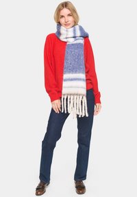 Blå og hvidstribet uldscarf med frynse detaljer, parret med en rød sweater og mørke jeans, i en minimalistisk indstilling.