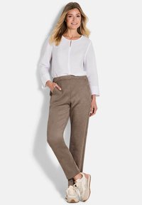 Lichte witte blouse met een sleutelgatdetail, gecombineerd met zachte bruine broek en sportieve beige sneakers. Gladde stof met een relaxte pasvorm.