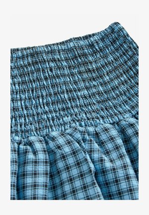 Jupe à carreaux bleu clair avec taille smockée. Présente un tissu texturé avec différents motifs de grille bleue et noire. Apparence douce et froncée.
