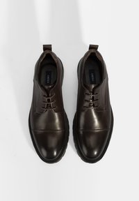 Bruine leren schoenen met een gladde afwerking, ronde neus en vetersluiting. Voorzien van een gestructureerde zool en een lus aan de hiel voor gemakkelijk aan- en uittrekken.