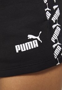 Gros plan sur un short noir avec le logo blanc Puma et une bande latérale noire et blanche estampillée Puma sur la cuisse d'une personne.