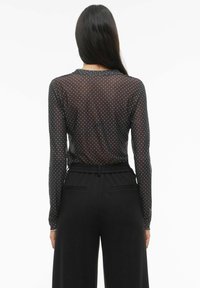 Czarna bluzka z długim rękawem w białe kropki, wykonana z przezroczystego materiału. Posiada okrągły dekolt i dopasowane rękawy, zestawiona z czarnymi szerokimi spodniami.