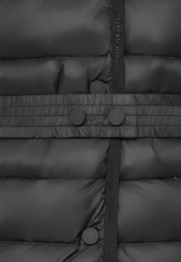 Svart puffjakke med quiltet design, med teksturert midjebånd og to runde knapper til lukking. Glatt, skinnende materiale.