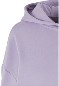 Hoodie lavande avec une texture douce et lisse, un col rond et une coupe décontractée avec une capuche structurée. Pas de motifs ni d'accents visibles.
