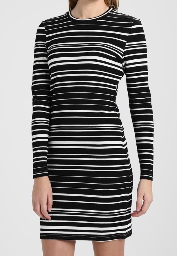 Femme portant une robe ajustée à rayures horizontales noires et blanches à manches longues avec un col rond.