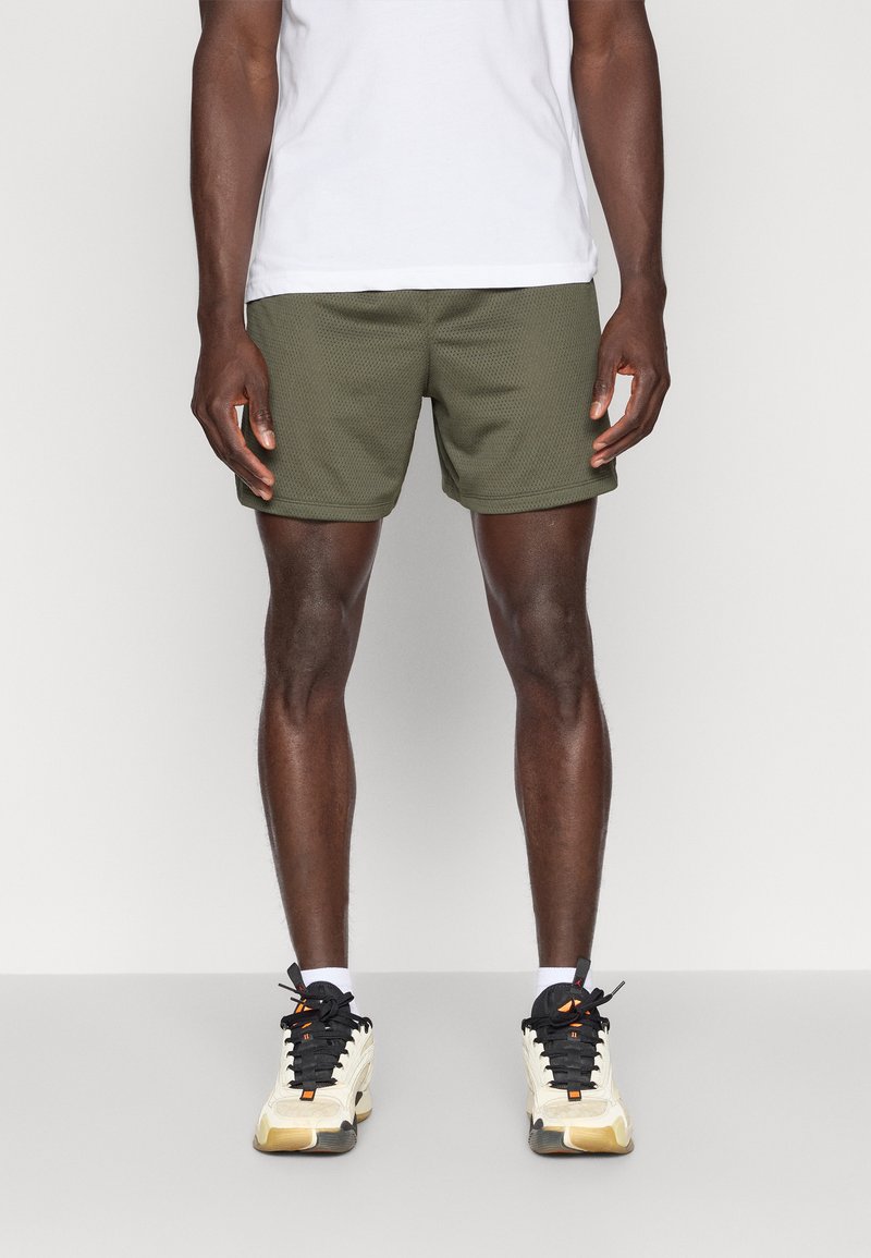 Αθλητικά σορτς ανδρικά σε ελαιόπρασινο, κατασκευασμένα από υφή ύφασμα. Συνδυασμένα με μαύρα και λευκά αθλητικά παπούτσια με πορτοκαλί λεπτομέρ ειες.