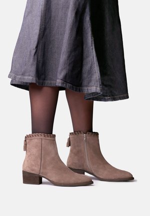 Bottes en suède marron montantes à la cheville, avec talons blocs et fermeture éclair sur le côté intérieur, portées avec des collants noirs transparents et une jupe en jean foncé.