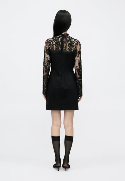 Svart kjole med en tettsittende silhuett, med lange gjennomsiktige blondermer og høy hals. Jevnt stoff på kroppen og blonde detaljer på ermene.