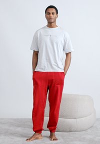 Γκρι κοντομάνικη μπλούζα με λογότυπο και κόκκινο παντελόνι φόρμας. Μαλακό ύφασμα, άνετη εφαρμογή, με ελαστικές μανσέτες και τσέπες. Χωρίς ορατά σχέδια.