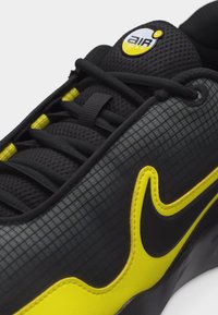 Κοντινή λήψη μαύρου και κίτρινου αθλητικού παπουτσιού Nike Air Max που δείχνει τη διχτυωτή γλώσσα, τα κορδόνια και το χαρακτηριστικό λογότυπο swoosh στην ανάγλυφη πλευρική επιφάνεια.