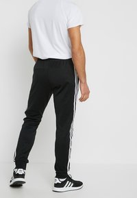 Svarta sportbyxor med vita sidostripes, elastiskt midjeband och åtsittande muddar. Kombinerade med en vit kortärmad skjorta och svarta sneakers.