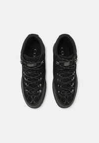 Schwarze Schnürschuhe mit einer strukturierten Oberseite, metallischen Ösen und einem runden Zehendesign. Die Sohle hat ein kontrastierendes Profil.