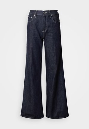 Traperice širokih nogavica u tamnom denimu, s visokim strukom, pet džepova, kontrastnim bijelim šavovima i glatkom teksturom.