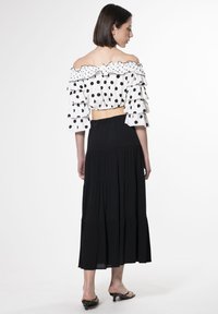 Ein schulterfreies Polka-Dot-Oberteil mit Rüschensäumen, kombiniert mit einem schwarzen gestuften Maxikleid. Glattes Material und eine taillierte Bundgestaltung.