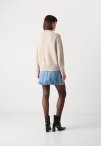 Beige gebreide trui met een hoge kraag, gecombineerd met een lichtblauwe denimrok en zwarte enkellaarsjes. De stof is glad met ribbelaccenten.