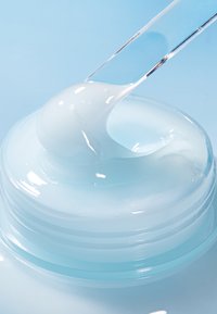 Kirkas geeli-voide läpinäkyvässä astiassa, jossa on sileä, kiiltävä pinta ja vaaleansininen väri, tiputin levittää sitä.