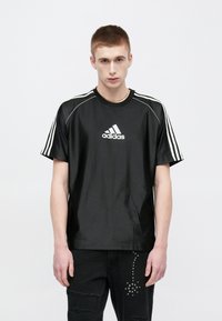 Μαύρο κοντομάνικο μπλουζάκι από λείο ύφασμα, με λευκό λογότυπο Adidas στο κέντρο και �τρεις λευκές ρίγες κατά μήκος των ώμων.