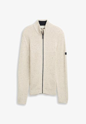 Kermanvärinen neuletakki, jossa on vetoketjukiinnitys, taitettu tekstuuri, korkea kaulus ja hienovaraisia täpliä. Mukana on musta yksityiskohta hihassa.