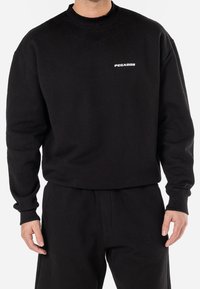 Black sweatshirt made of cotton blend, featuring a crew neck and long sleeves. White "PEGADOR" logo on the chest. Soft, textured fabric.