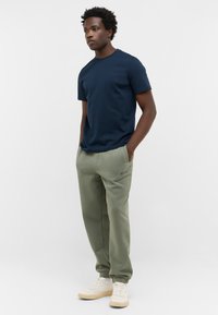 Granatowa bawełniana koszulka z okrągłym dekoltem, zestawiona z oliwkowymi joggerami z bocznymi kieszeniami; noszona z białymi trampkami.