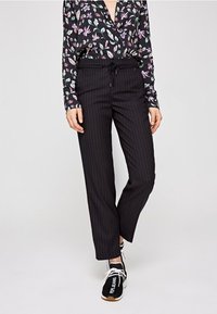 Pantaloni neri a righe con una vita elastica e cordino, abbinati a una blusa a stampa floreale nei toni del nero, bianco e pastello.