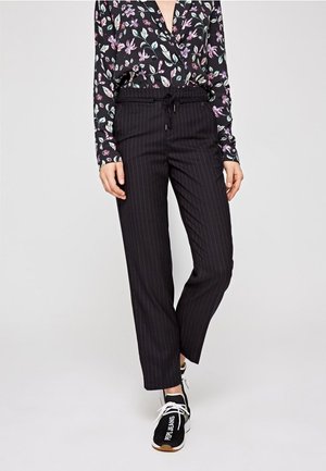 Pantaloni neri a righe con una vita elastica e cordino, abbinati a una blusa a stampa floreale nei toni del nero, bianco e pastello.