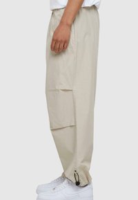 Beige, lette cargo bukser med elastisk talje og justerbare manchetter, der har sidelommer og en glat, mat tekstur.