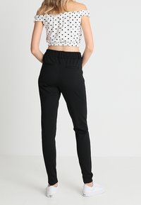 Pantaloni neri con fascia elastica in vita, slim fit. Abbinati a una maglietta bianca a spalle scoperte con pois. Sneakers bianche. Design minimalista e texture liscia.