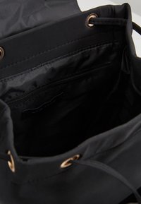 Czarna torba na sznurek o gładkiej, matowej fakturze, wyposażona w złote oczka. Wnętrze wyłożone czarną tkaniną z kieszenią na zamek.