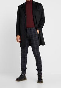 Czarny wełniany płaszcz na bordowym golfie, zestawiony z ciemnymi spodniami w kratę i czarnymi botkami na sznurowadła. Charakteryzuje się dopasowanym krojem i eleganckim wyglądem.