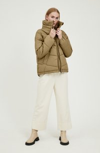 Giacca puffer khaki con colletto alto, texture trapuntata e chiusura con zip. Abbinata a pantaloni larghi di colore crema e stivaletti beige.