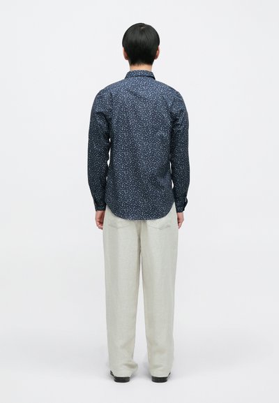 Μπλε σκούρο πουκάμισο με κουμπιά και μικρό λουλουδένιο μοτίβο, μακριά μανίκια και στρογγυλεμένο τελείωμα, φορεμένο με ανοιχτόχρωμο, φαρδύ παντελόνι.